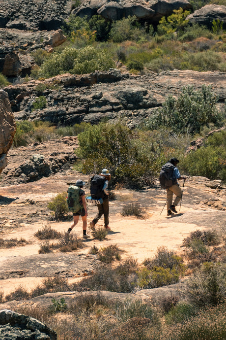 Three hikers with backpacks walking on a rocky trail in a rugged landscape.